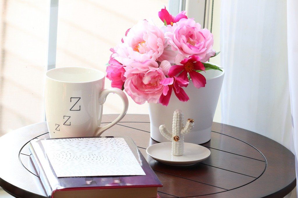 Pink peonies, a white mug, a book and a cactus ring holder on a small round table
