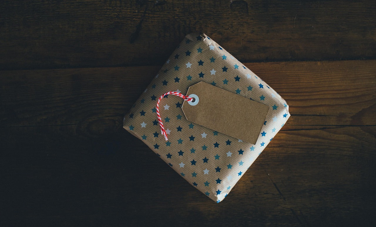 A brown paper wrapped gift with a blank kraft gift tag resting on a dark wood table