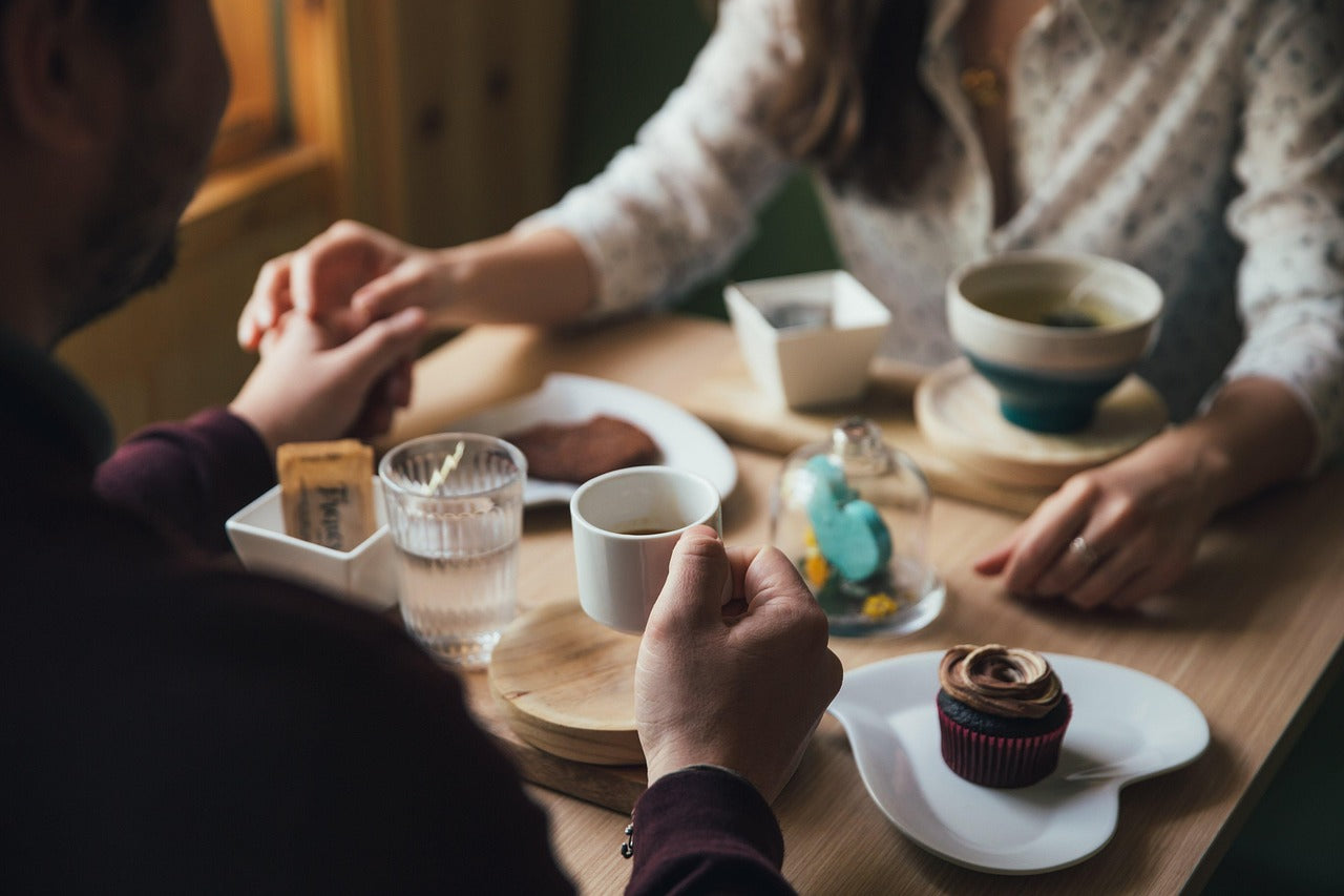 Two people holding hands across a small cafe table with coffee and dessert