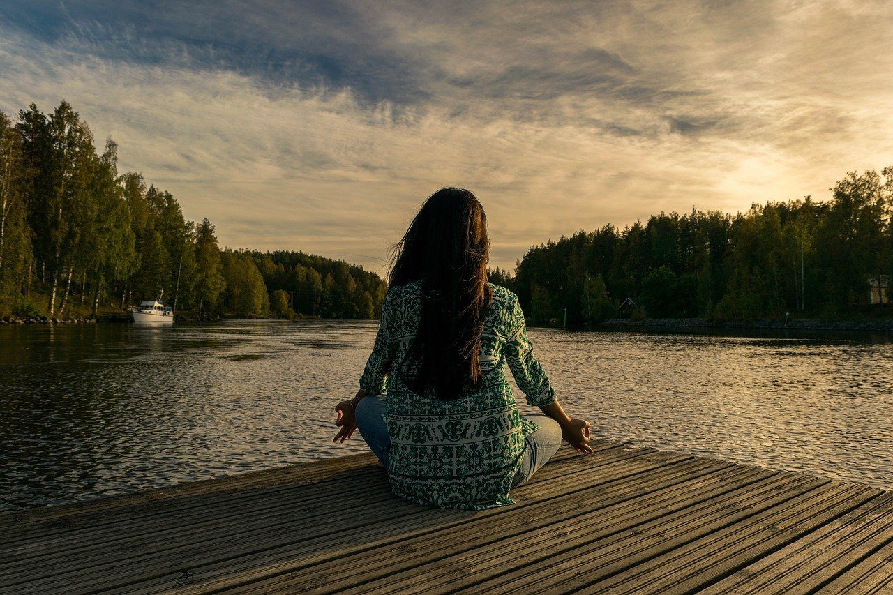 Woman meditating on a wooden dock by a lake at sunset