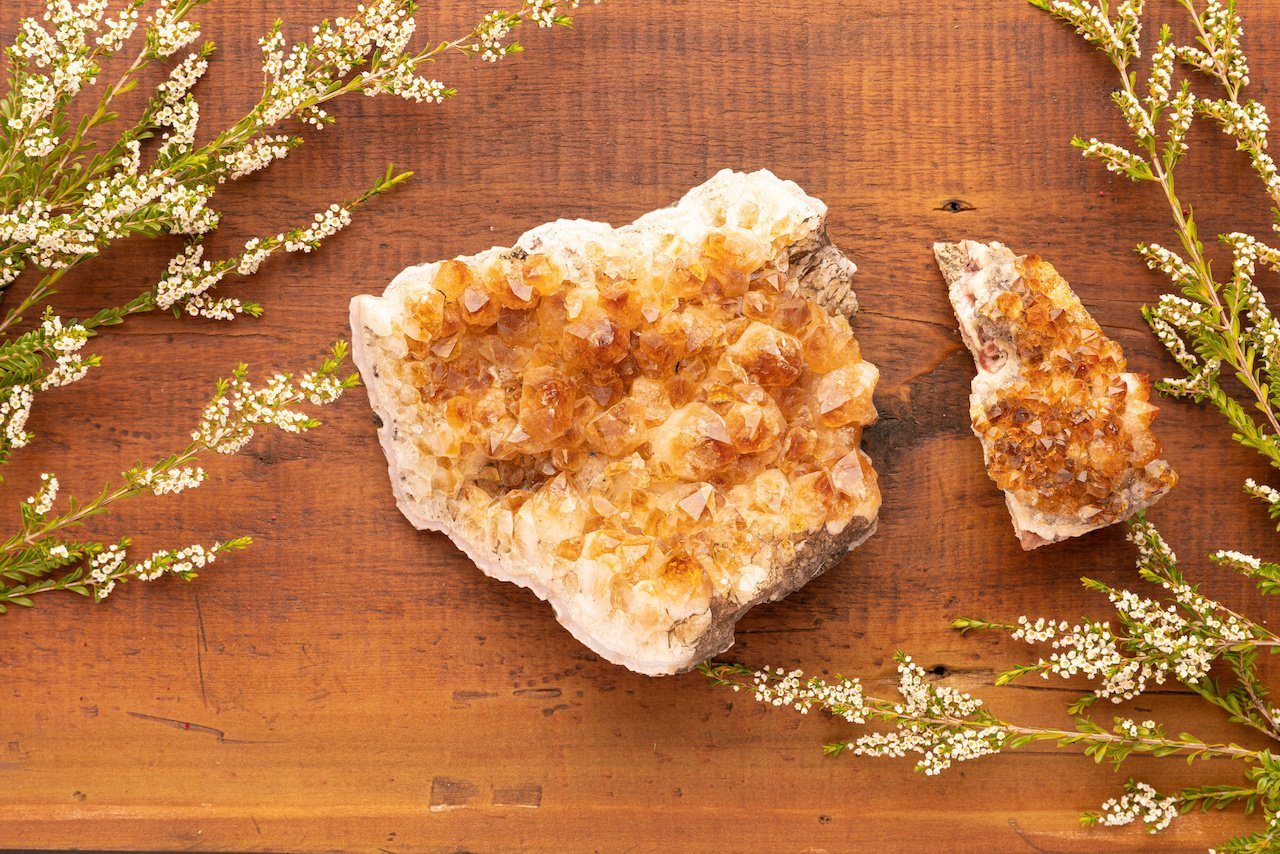Golden citrine crystal clusters on a wooden table beside sprigs of small white flowers
