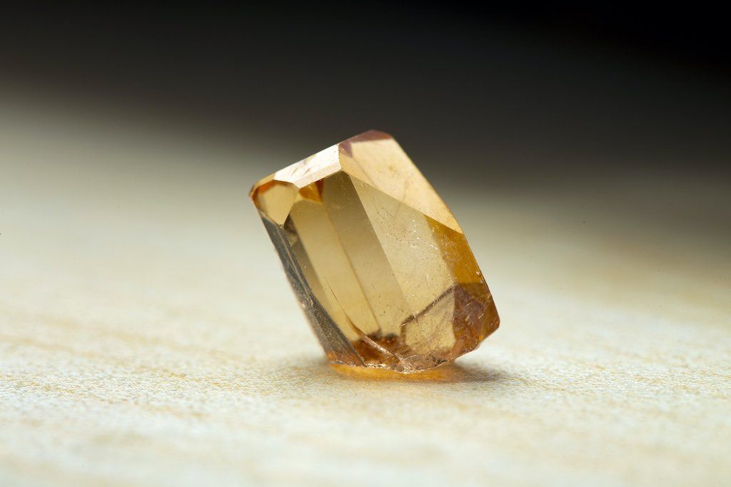 Faceted golden topaz gemstone on a pale surface