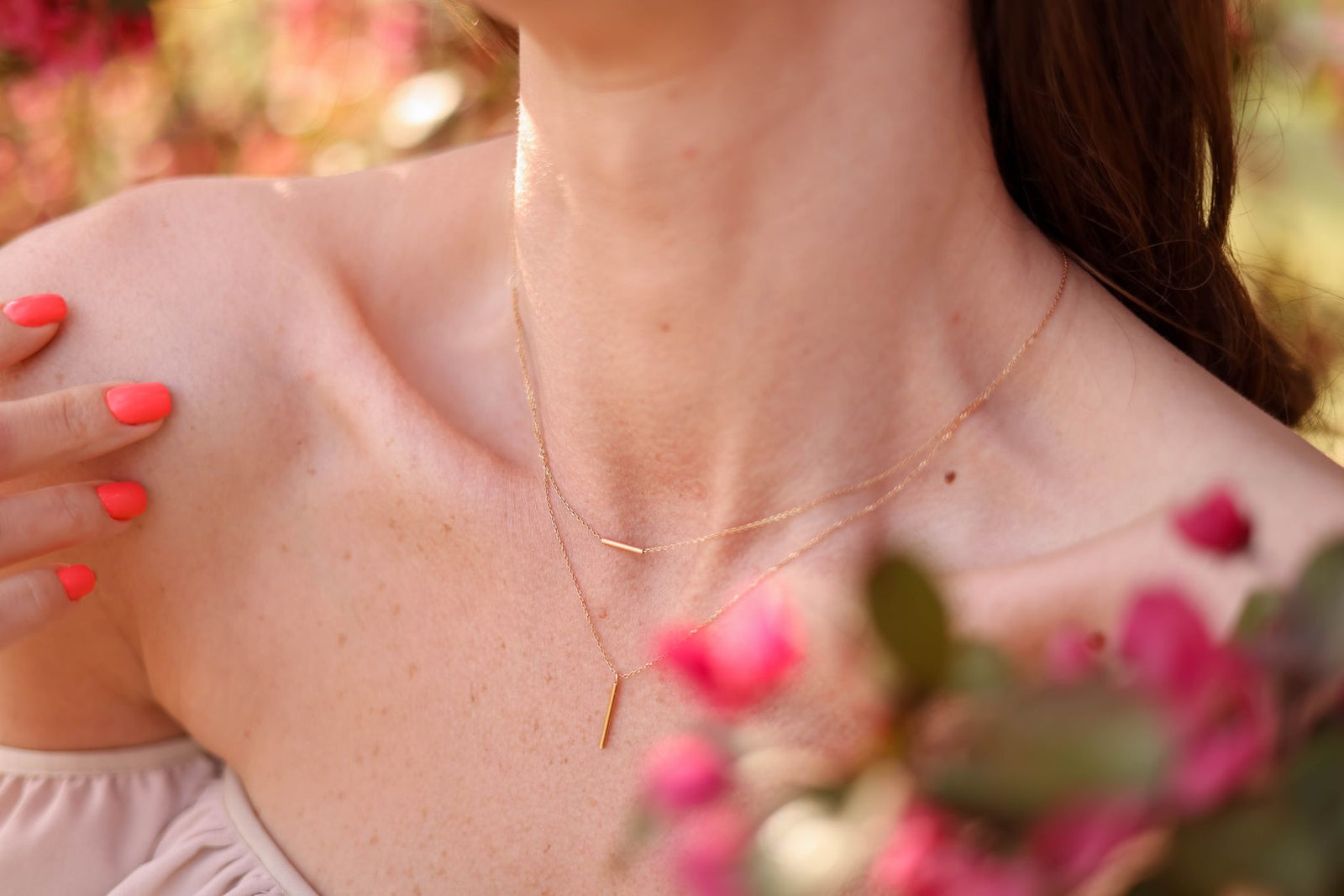 Close view of a delicate gold necklace on a woman's collarbone beside pink flowers
