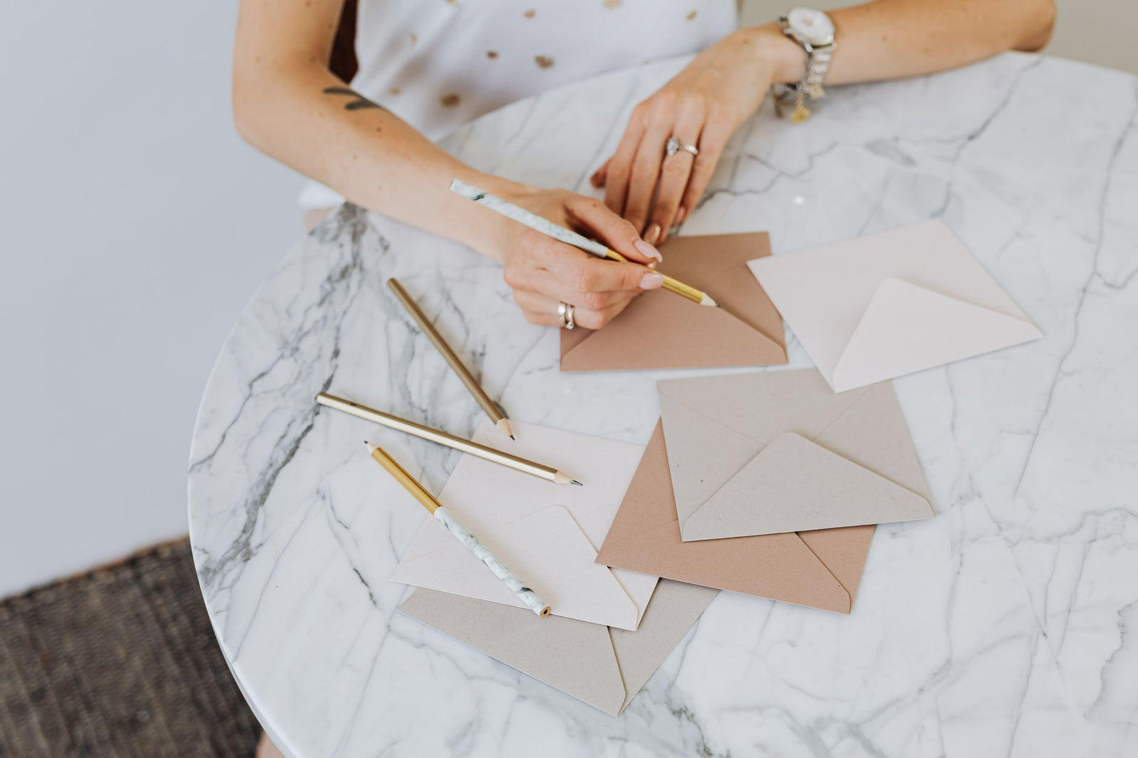 A woman writing on kraft paper envelopes at a white marble table