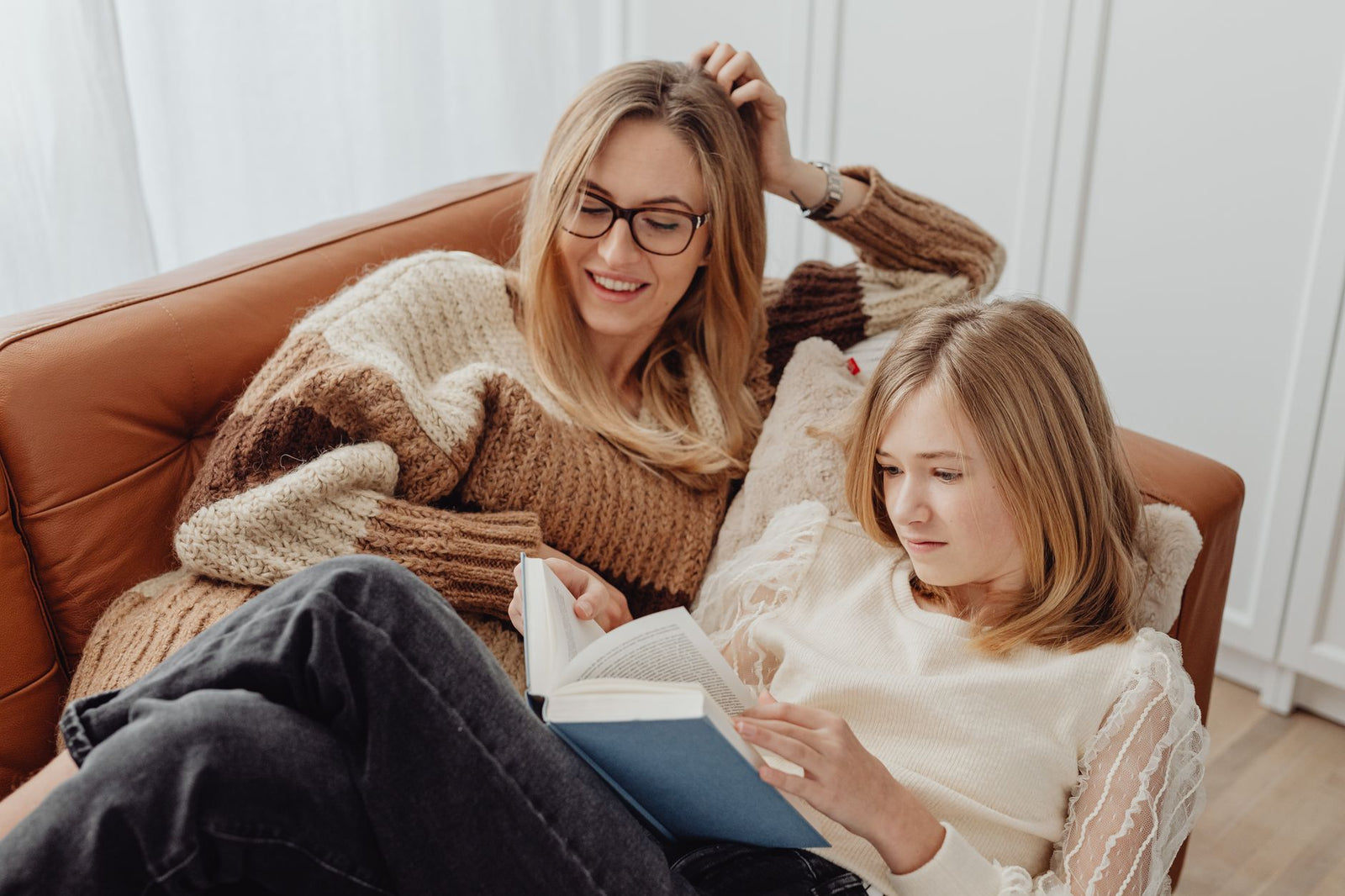 A mother and her teenage daughter reading together on a sofa at home