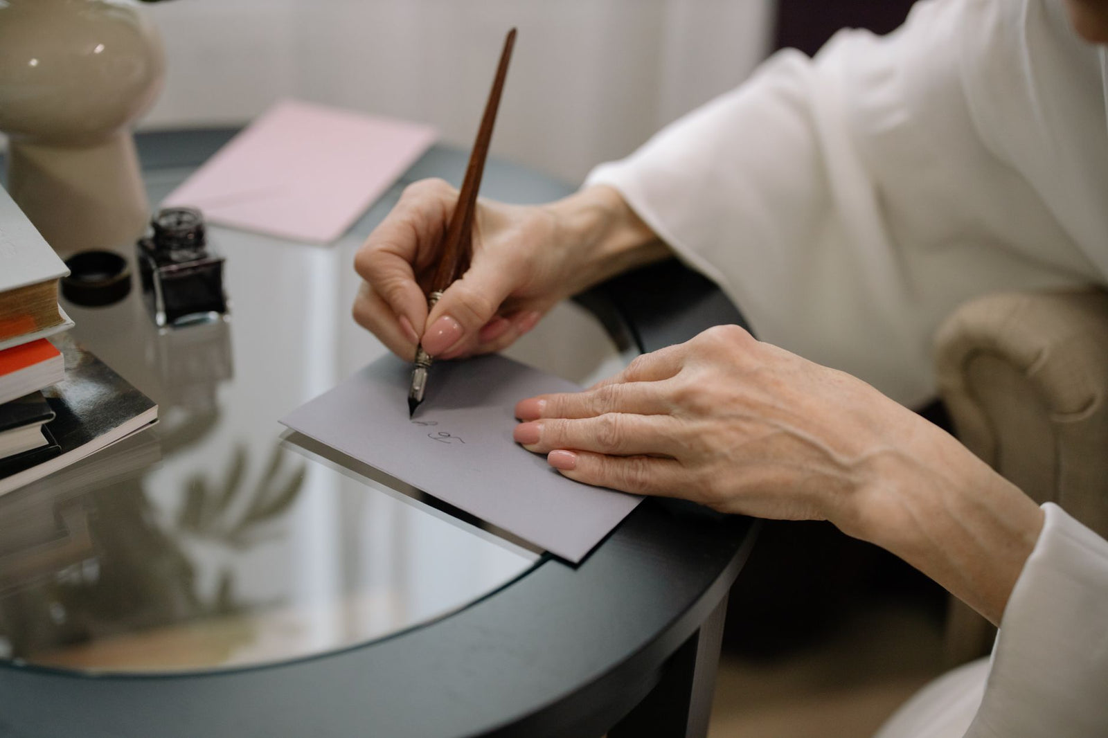 Hands writing on a gray envelope with a fountain pen at a small desk