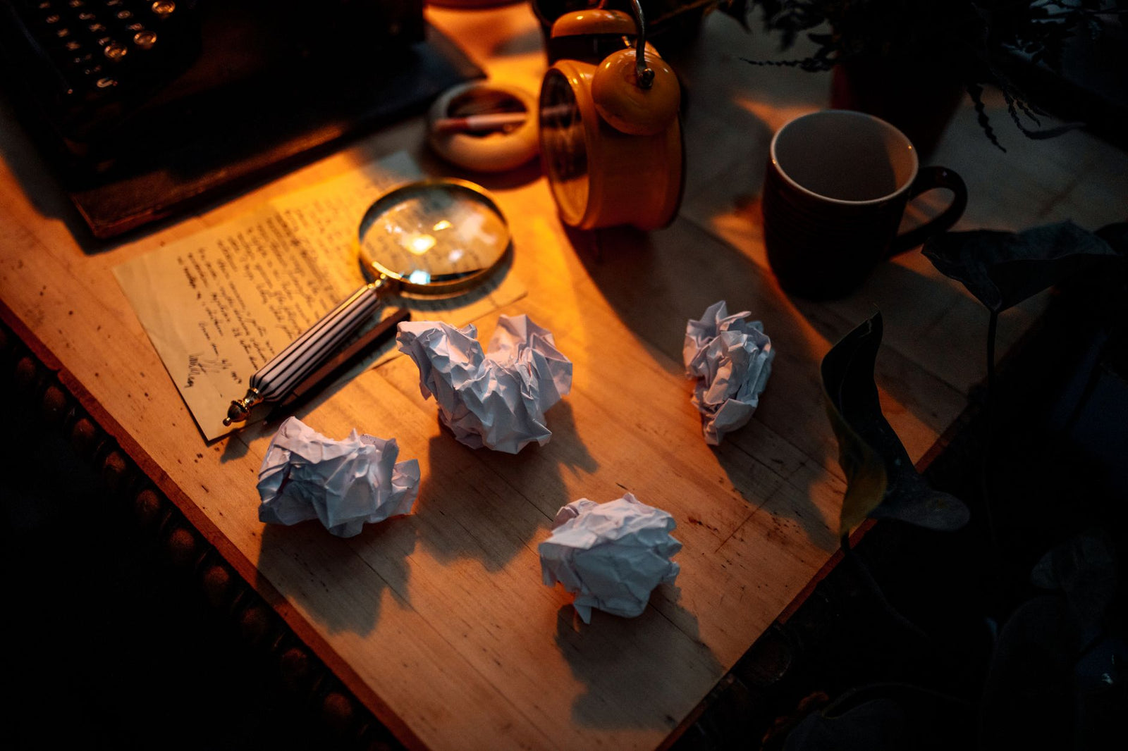 A writing desk with crumpled paper, a warm lamp and a mug of coffee