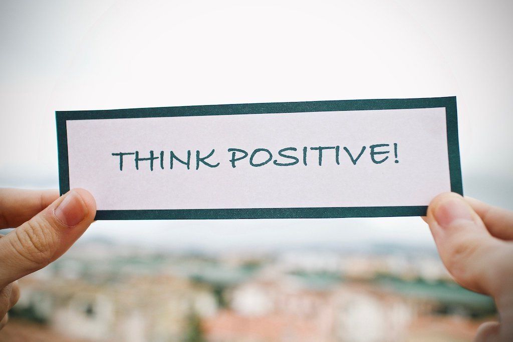 Two hands holding up a paper card that reads Think Positive